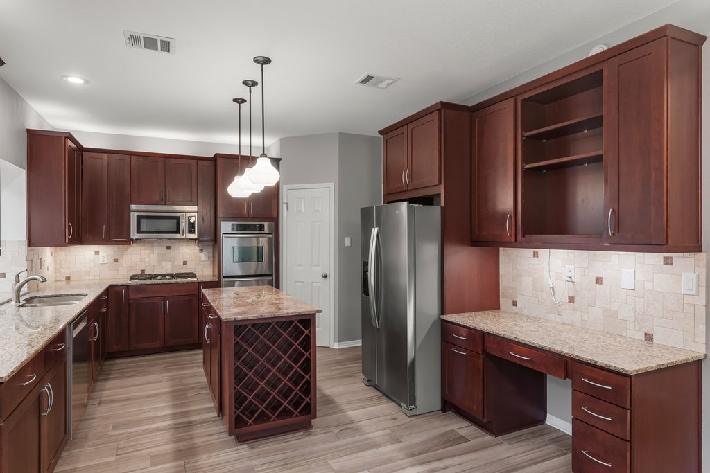 1406 Dapplegrey Lane Austin, TX 78727 - Photo 8 of 38 Kitchen featuring light stone countertops, stainless steel appliances, tasteful backsplash, open shelves, and a center island