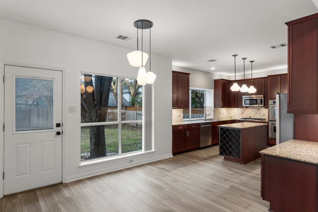 1406 Dapplegrey Lane Austin, TX 78727 - Photo 9 of 38 Kitchen featuring a kitchen island, stainless steel appliances, pendant lighting, light stone counters, and tasteful backsplash