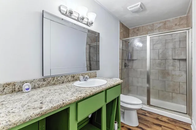 a bathroom with a granite countertop sink a toilet a mirror and shower