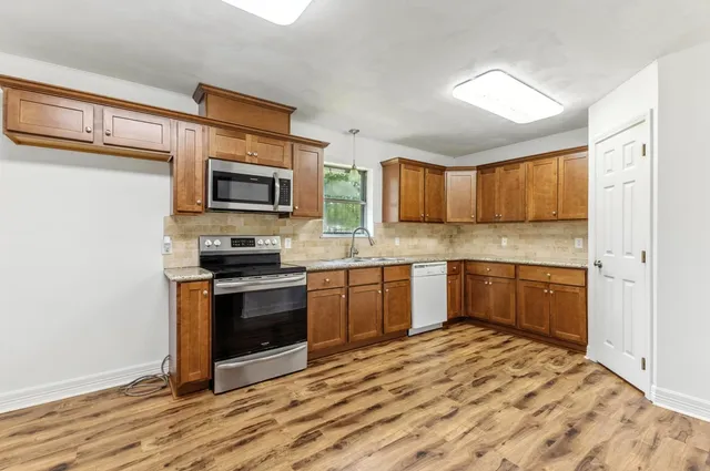 a kitchen with stainless steel appliances granite countertop a stove top oven a sink dishwasher a refrigerator and a microwave oven with wooden floor