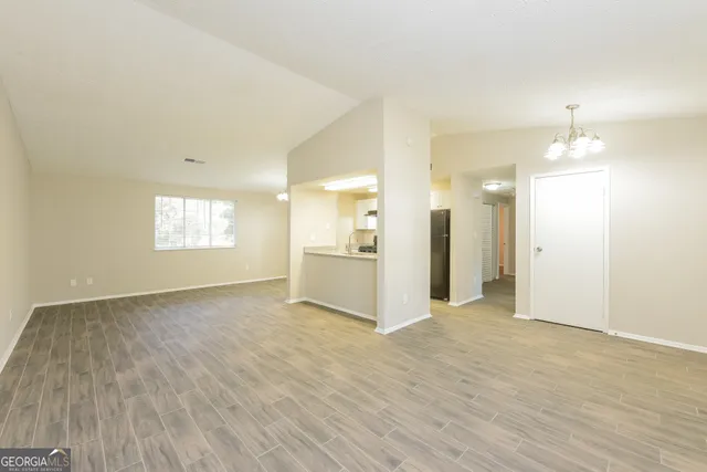 an empty room with wooden floor and kitchen view