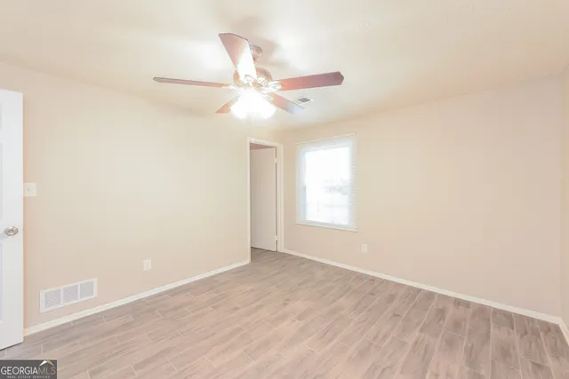 an empty room with wooden floor fan and windows