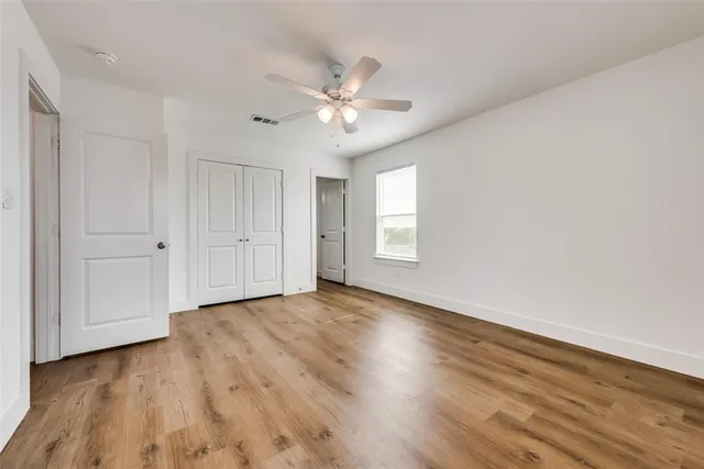 an empty room with wooden floor fan and windows