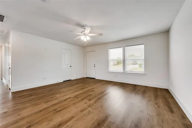 an empty room with wooden floor chandelier fan and windows
