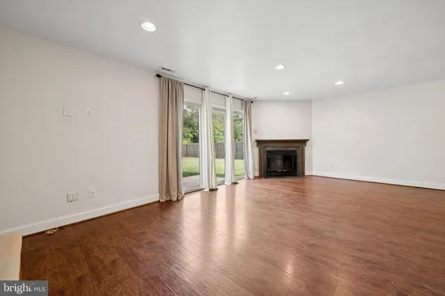 an empty room with wooden floor fireplace and windows