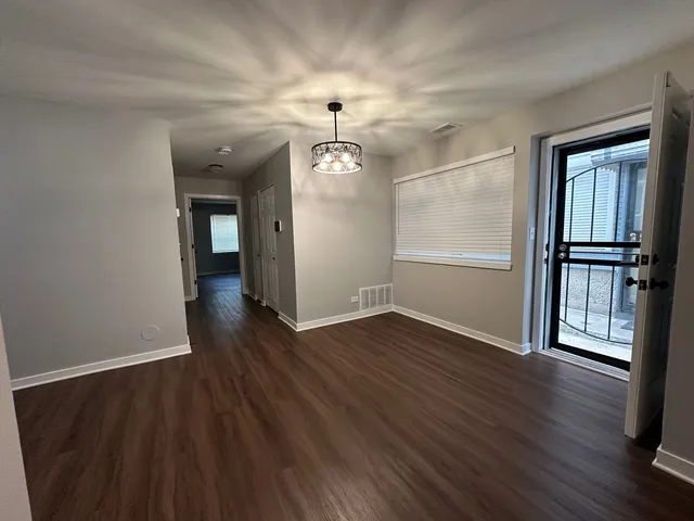 an empty room with wooden floor chandelier and windows