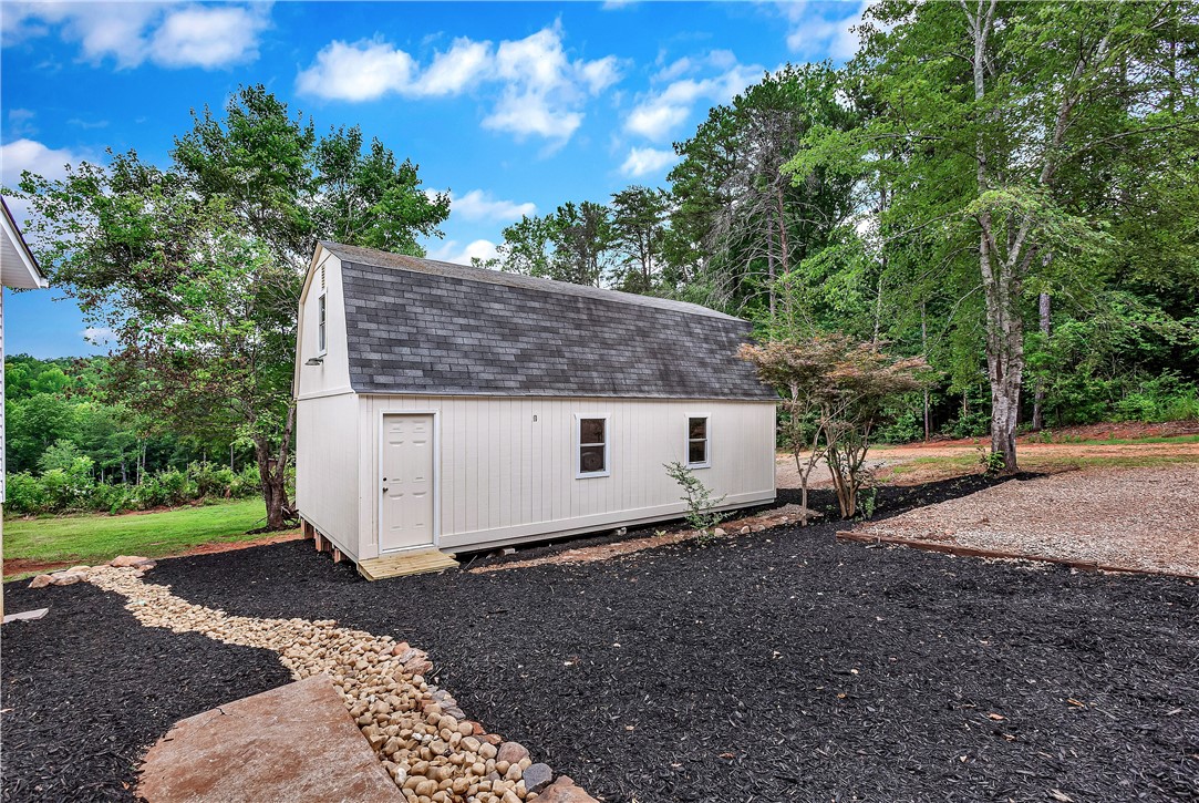 403 Hancox Place Westminster, SC 29693 - Photo 13 of 39 A quaint barn-style shed, nestled amidst lush greenery, offers versatile outdoor storage.