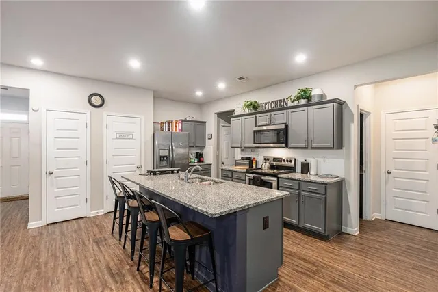 a kitchen with stainless steel appliances granite countertop a stove top oven a sink dishwasher and a refrigerator with wooden floor