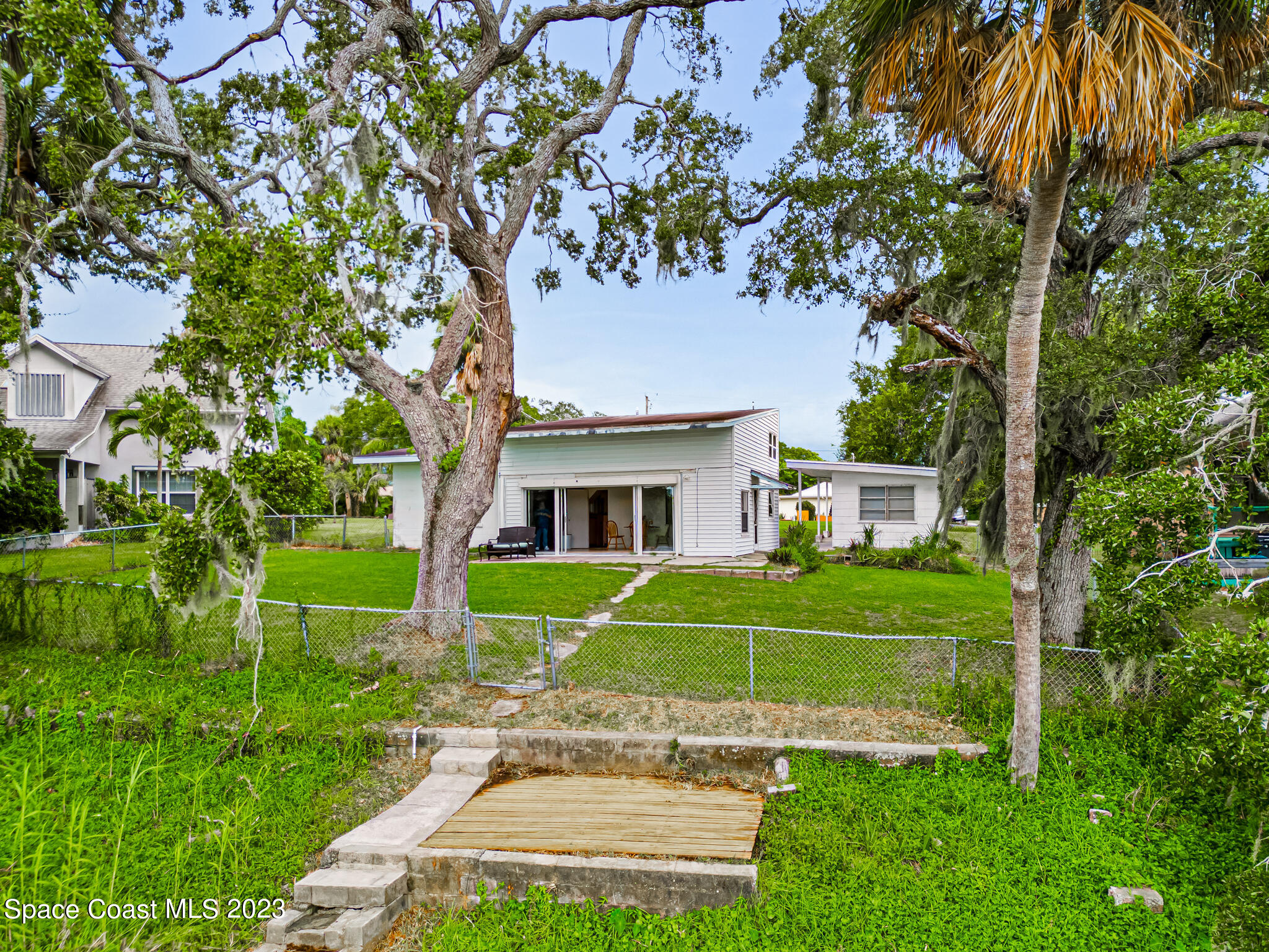 877 Sunset Drive Melbourne, FL 32935 - Photo 37 of 49 a view of a white house in front of a big yard with plants and large trees