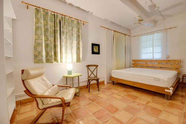 a bedroom with a bed chair and two windows