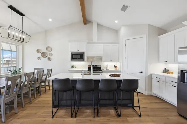 a kitchen with stainless steel appliances kitchen island granite countertop a dining table chairs and white cabinets