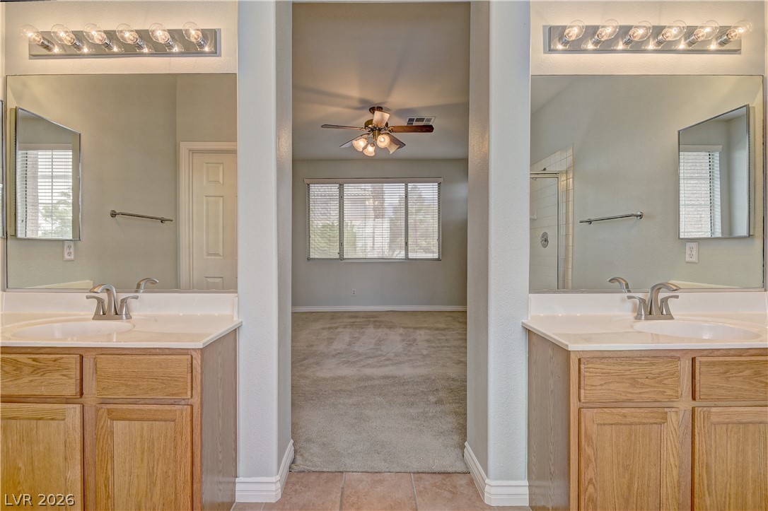 1813 Snow Spring Lane Las Vegas, NV 89134 - Photo 27 of 37 Twin vanities frame a hallway leading to a bright, window-filled primary bedroom.