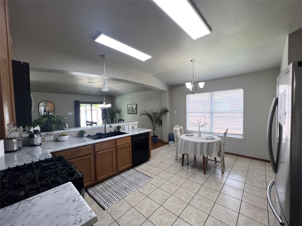 404 Patton Cove Bastrop, TX 78602 - Photo 3 of 40 Kitchen featuring lofted ceiling, a new modern sink and new faucet , black & stainless appliances, brown cabinetry, and a notable chandelier
