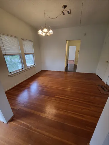 a view of an empty room with wooden floor and a chandelier