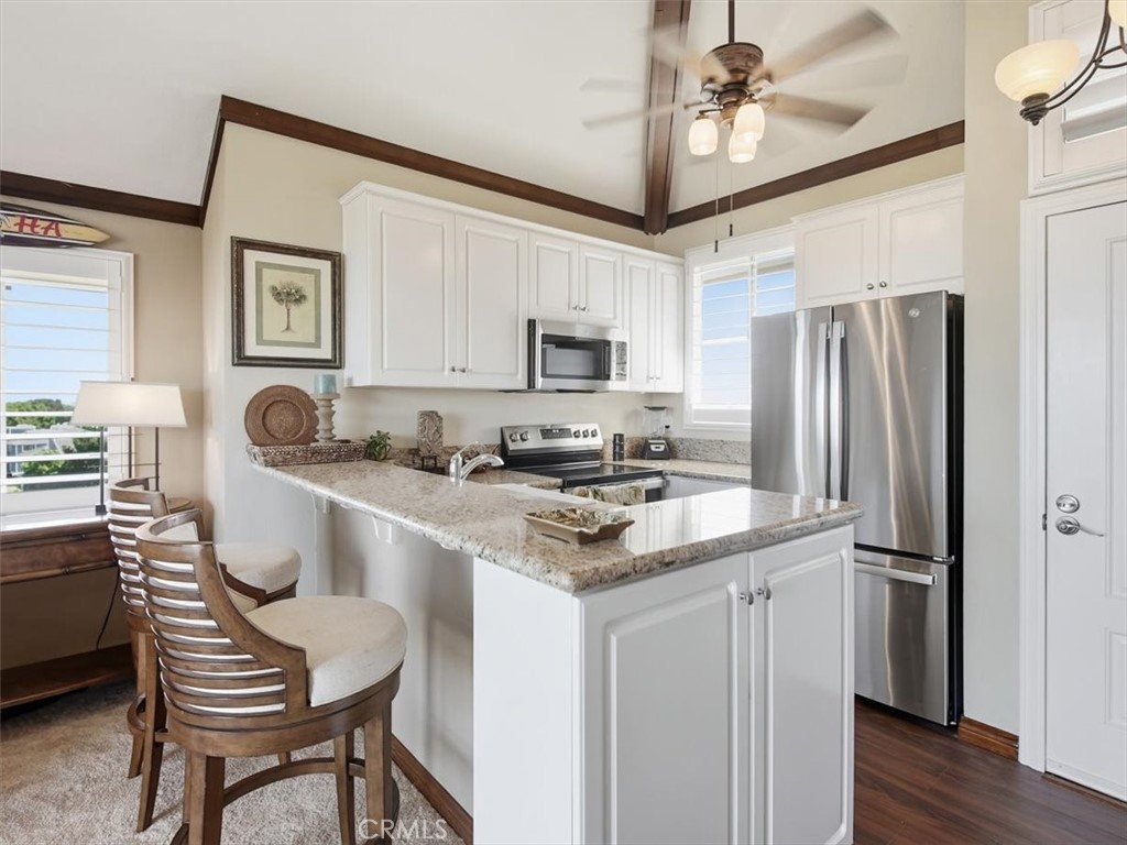 20331 Bluffside Circle, Unit A411 Huntington Beach, CA 92646 - Photo 4 of 44 a kitchen with stainless steel appliances granite countertop a sink stove a refrigerator a microwave oven with white cabinets and wooden floor