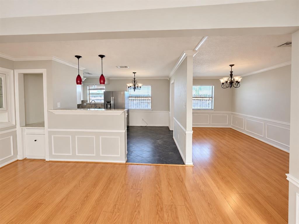 17922 Hillcrest Road Dallas, TX 75252 - Photo 4 of 11 Wood-finish flooring throughout, wainscoting details, built-in cabinetry, modern pendant lighting, and a stainless steel refrigerator