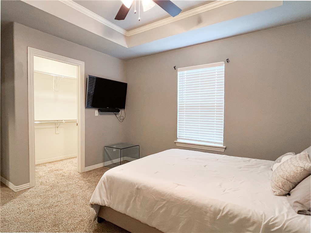 1275 North Rupple Road Fayetteville, AR 72704 - Photo 18 of 20 Carpeted bedroom featuring a tray ceiling with a ceiling fan, a window with blinds, and a doorway opening to a walk-in closet with built-in shelving