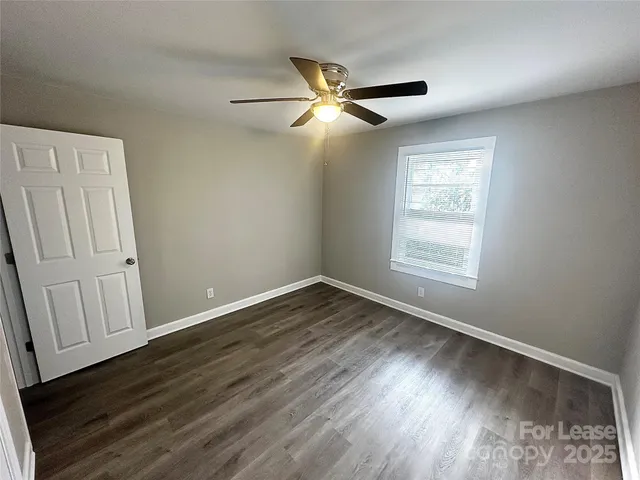 an empty room with wooden floor fan and windows