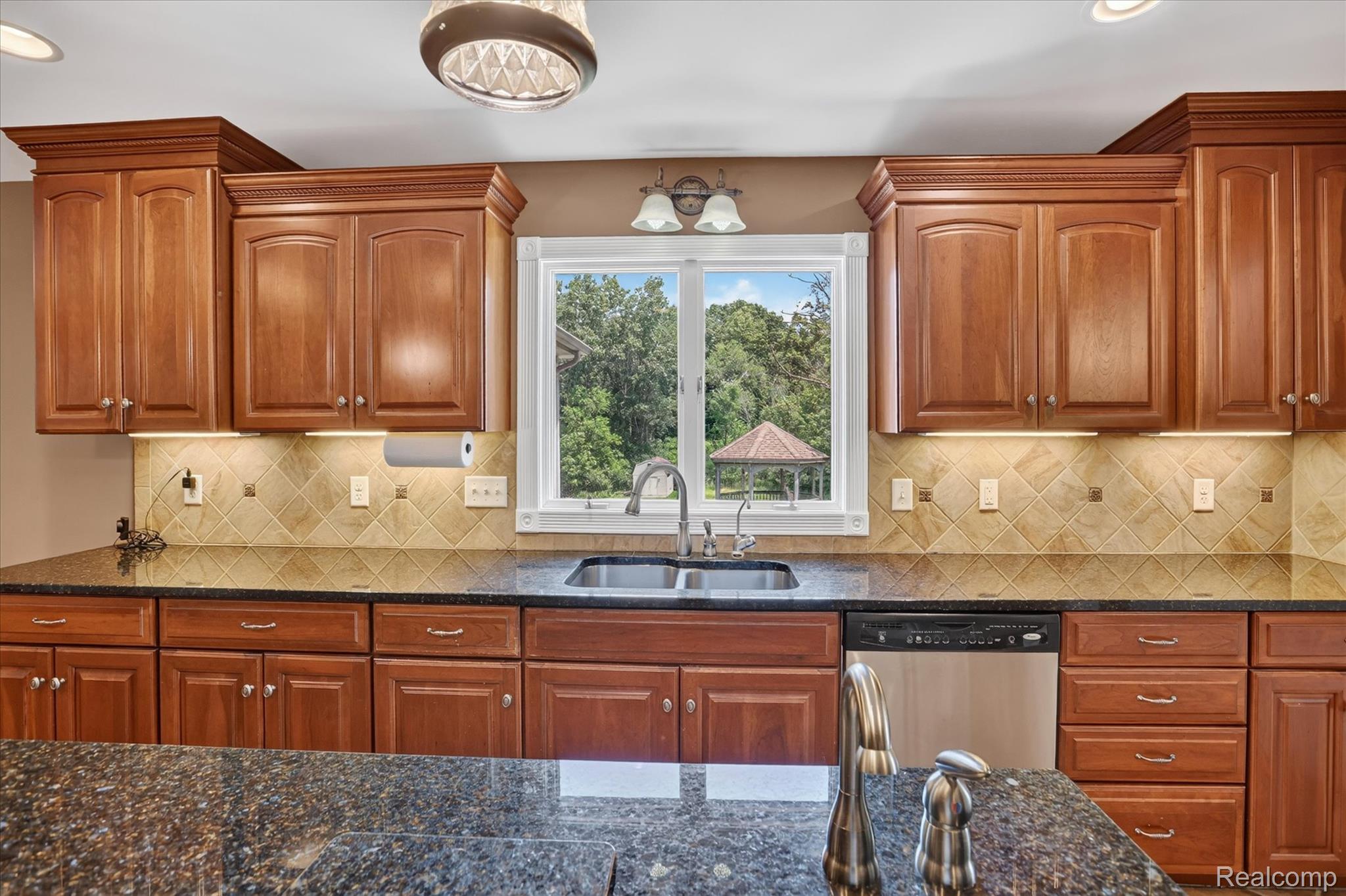 7186 East River Road Flushing, MI 48433 - Photo 10 of 47 Kitchen featuring extensive wood cabinetry with crown molding, dark stone countertops, stainless steel appliances, and a tile backsplash