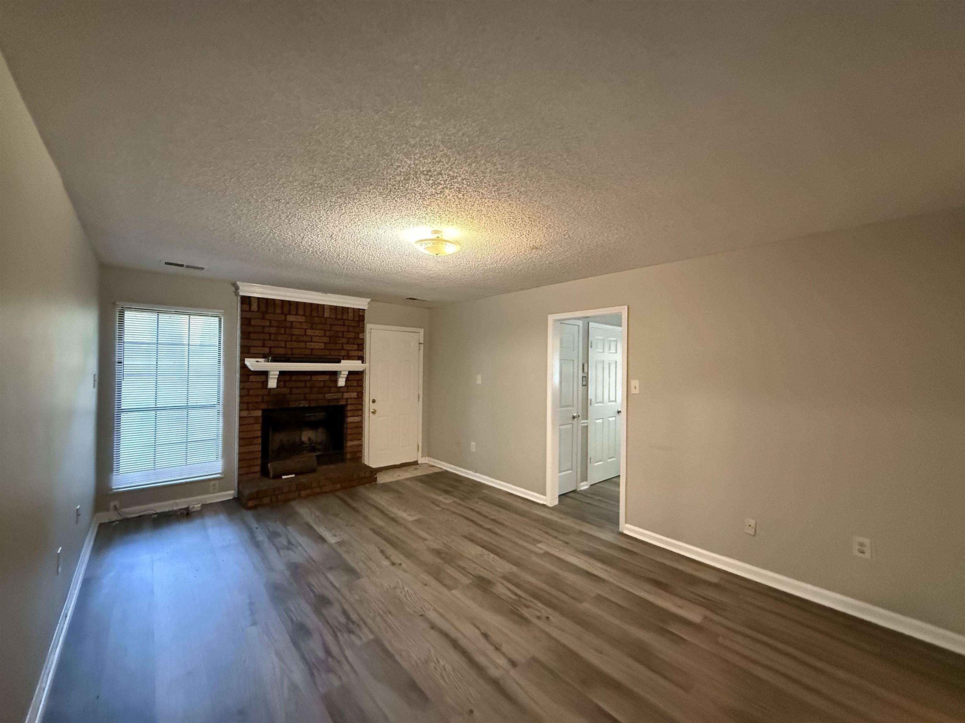 6420 Saginaw Road Memphis, TN 38134 - Photo 13 of 38 Spacious room featuring wood-finish flooring, a brick fireplace with a white mantel, and neutral wall tones