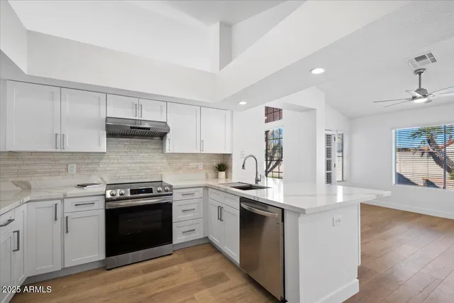 a kitchen with stainless steel appliances granite countertop a stove top oven a sink dishwasher and white cabinets with wooden floor