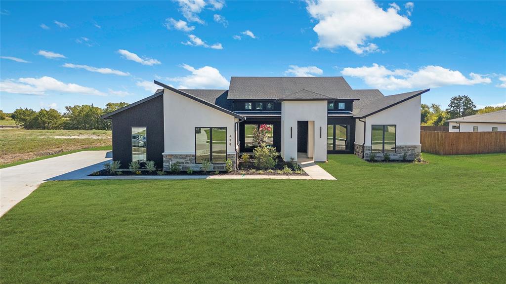 430 Whispering Way Red Oak, TX 75154 - Photo 5 of 40 Modern architectural exterior featuring a striking black and white facade, large windows, a contrasting stone base, a dark shingle roof, and a concrete driveway
