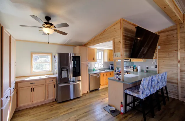 a kitchen with a refrigerator a sink dishwasher a dining table and chairs with wooden floor