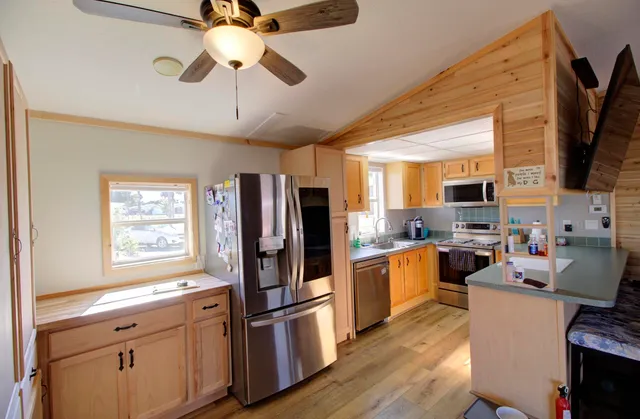 a kitchen with stainless steel appliances a refrigerator a stove top oven a sink a dining table and chairs with wooden floor