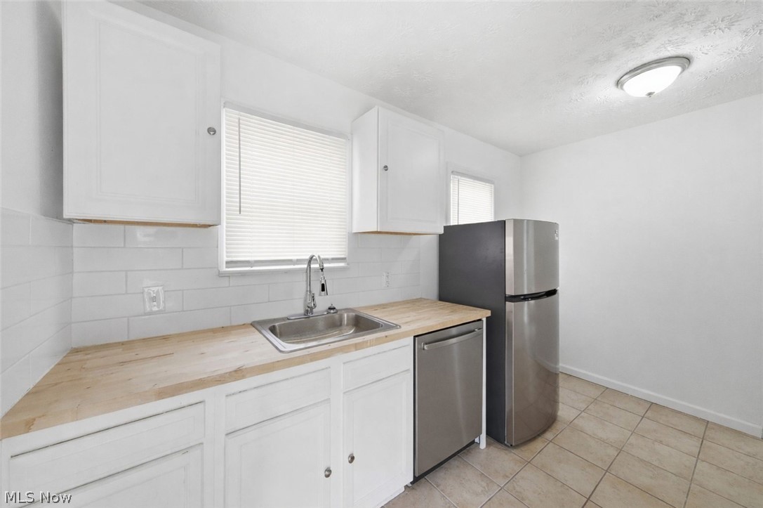 20705 Hansen Road Maple Heights, OH 44137 - Photo 6 of 24 Kitchen featuring butcher block counters, white cabinetry, stainless steel appliances, backsplash, and a textured ceiling
