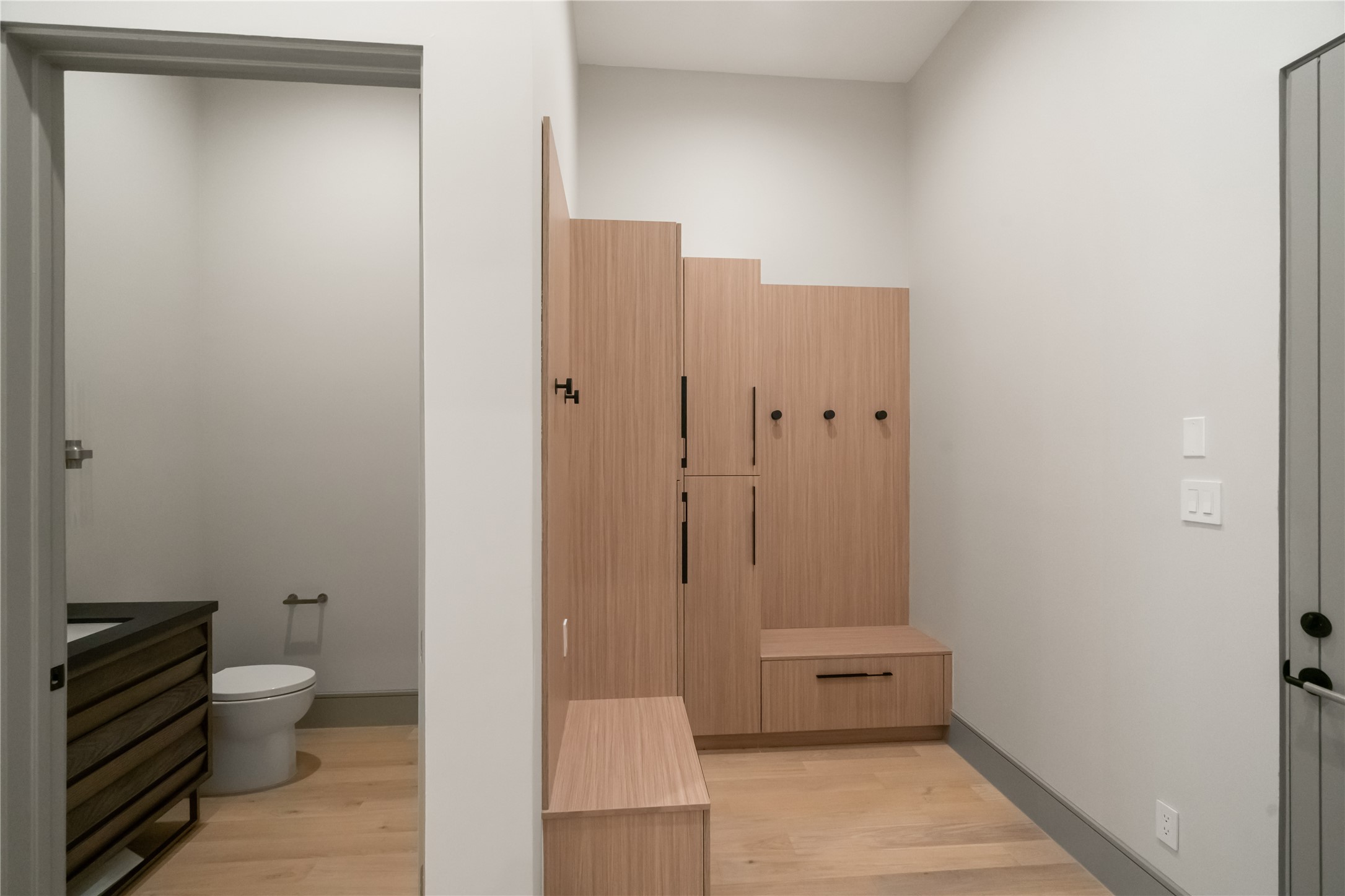 47 Pronghorn Place Spring, TX 77389 - Photo 38 of 44 This photo shows a modern mudroom with light wood lockers and hooks for storage. Adjacent is a small bathroom with a toilet and a sleek vanity, featuring light wood flooring throughout.