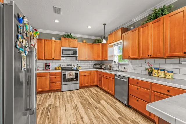 a kitchen with stainless steel appliances granite countertop a refrigerator a sink dishwasher a stove and white countertops with wooden floor