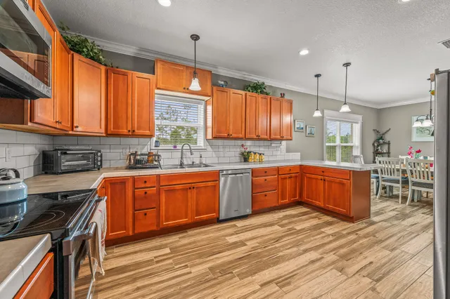 a kitchen with stainless steel appliances granite countertop wooden cabinets a sink a stove a dining table and chairs