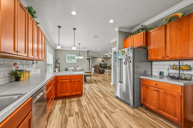 a kitchen with stainless steel appliances granite countertop a refrigerator a sink dishwasher a stove and white countertops with wooden floor