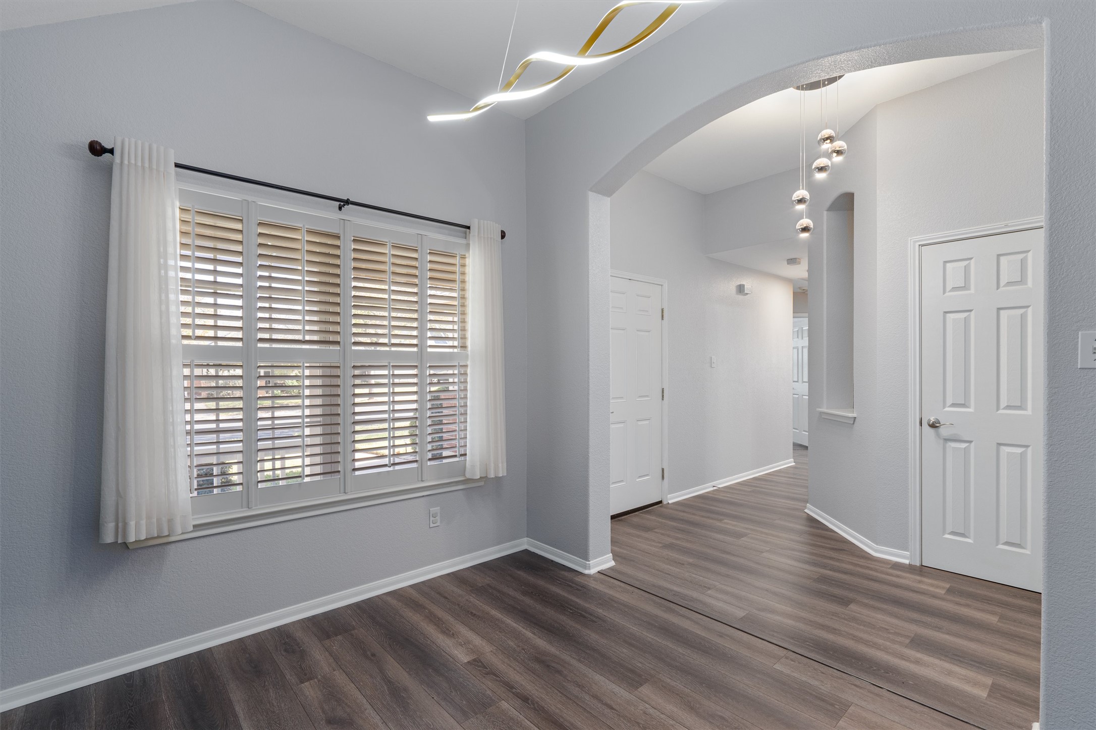 153 Hickory Lane Georgetown, TX 78633 - Photo 4 of 30 Spacious room featuring wood-finish flooring, white plantation shutters, and a contemporary linear chandelier