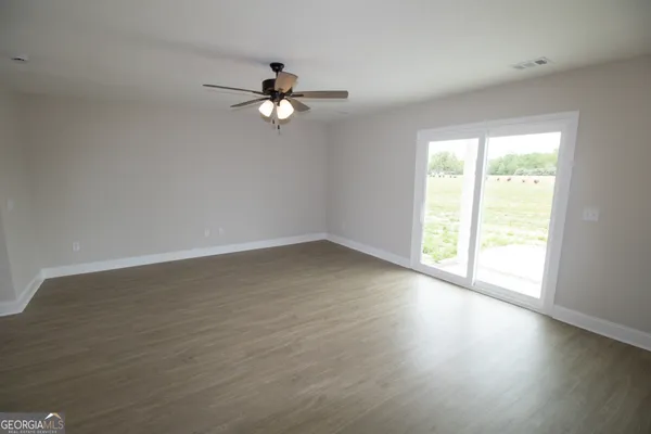 an empty room with wooden floor fan and windows