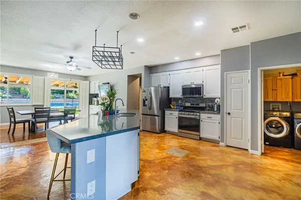 a kitchen with stainless steel appliances kitchen island granite countertop a stove top oven a sink a dining table and chairs with wooden floor
