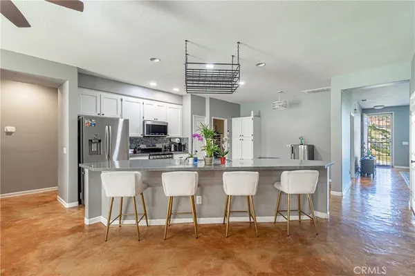 a kitchen with stainless steel appliances kitchen island granite countertop a dining table chairs and a refrigerator