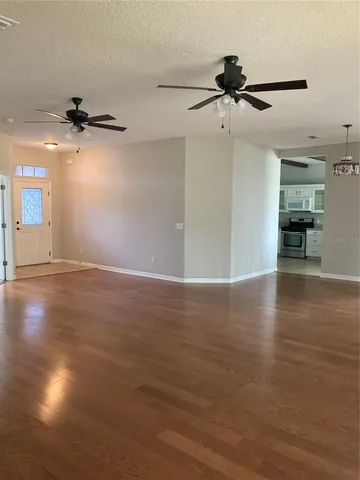 an empty room with wooden floor ceiling fan and windows