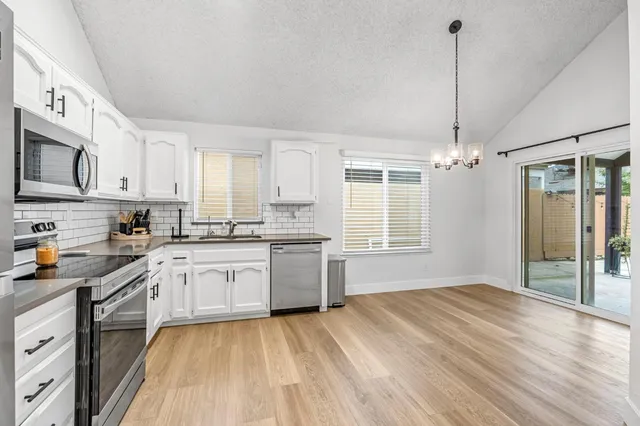 a kitchen with stainless steel appliances granite countertop a sink dishwasher stove and white cabinets with wooden floor