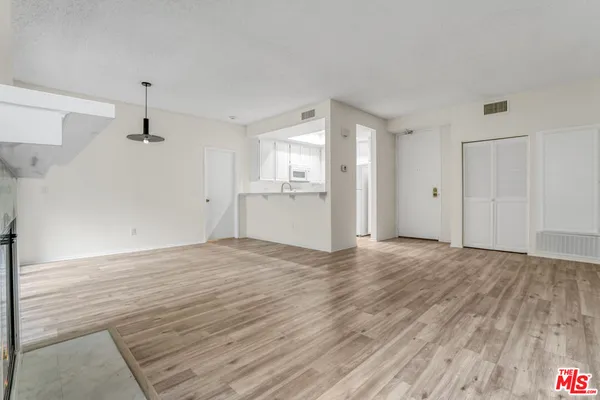 a view of empty room with wooden floor and kitchen