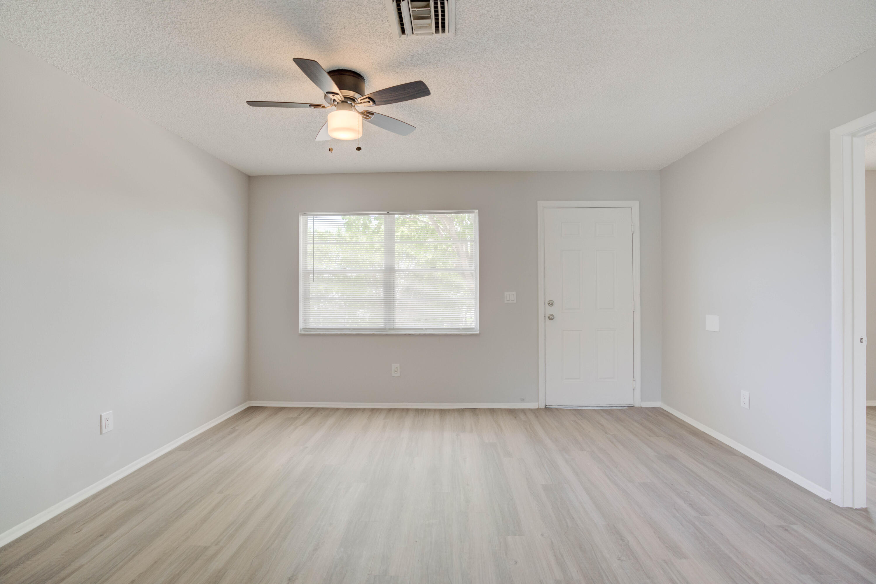 6610 Jupiter Gardens Boulevard, Unit F Jupiter, FL 33458 - Photo 13 of 14 an empty room with wooden floor chandelier fan and windows