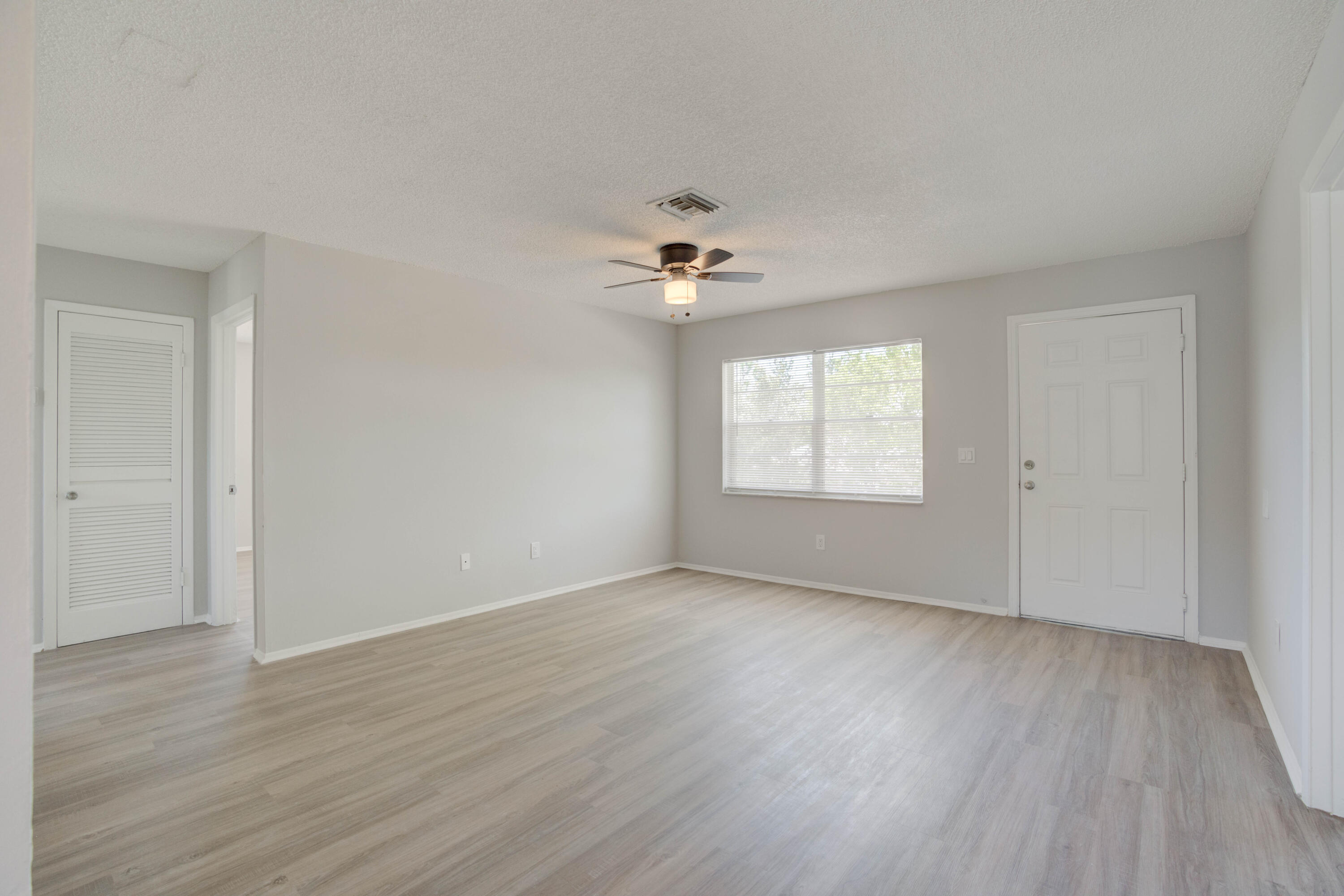 6610 Jupiter Gardens Boulevard, Unit F Jupiter, FL 33458 - Photo 5 of 14 an empty room with wooden floor chandelier fan and windows