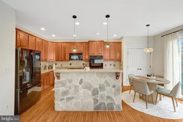 a large kitchen with stainless steel appliances kitchen island granite countertop a refrigerator a stove a sink a dining table and chairs with wooden floor
