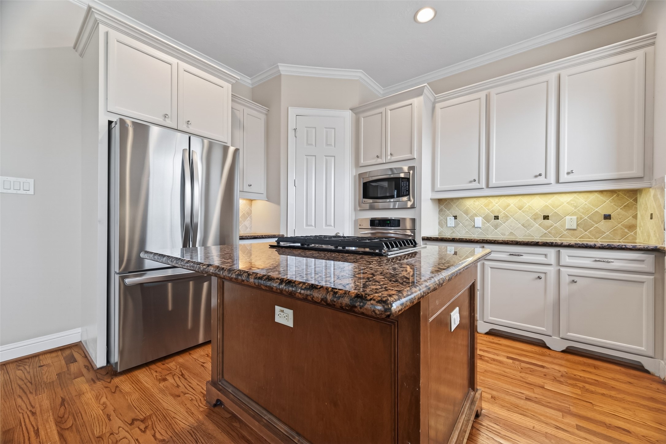 2611 Riverside Drive, Unit C Houston, TX 77004 - Photo 15 of 50 This kitchen features stainless steel appliances, granite countertops, and a central island with a cooktop. It has ample cabinetry, a built-in microwave, and warm hardwood flooring, creating a modern and functional space.