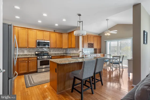 a kitchen with stainless steel appliances granite countertop a stove top oven a sink dishwasher a dining table and chairs with wooden floor