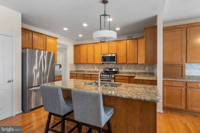 a kitchen with stainless steel appliances granite countertop a refrigerator a stove top oven a sink dishwasher a dining table and chairs with wooden floor