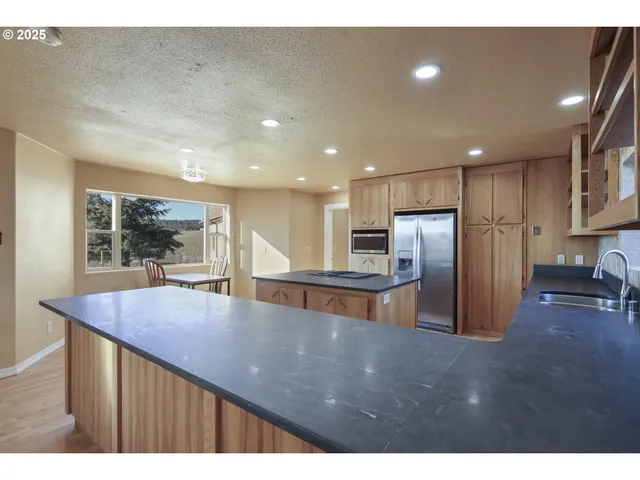 a open kitchen with stainless steel appliances granite countertop a refrigerator a sink a stove and a center island with wooden floor