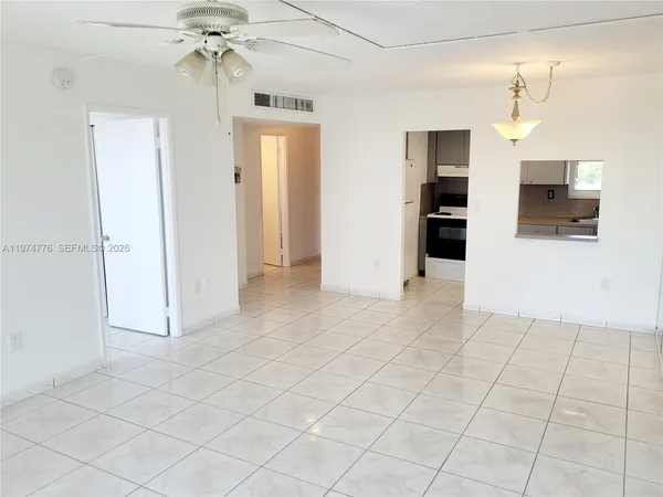 an empty room with chandelier fan and kitchen view