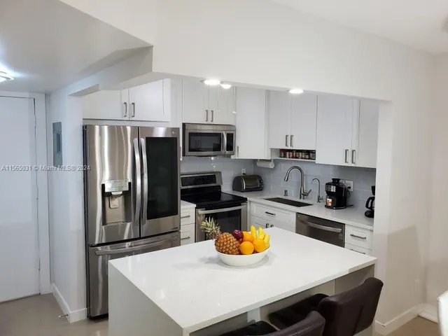a kitchen with stainless steel appliances a sink a stove a refrigerator cabinets and chairs
