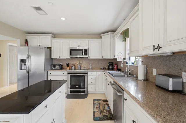 a kitchen with granite countertop a sink a counter top space stainless steel appliances and cabinets